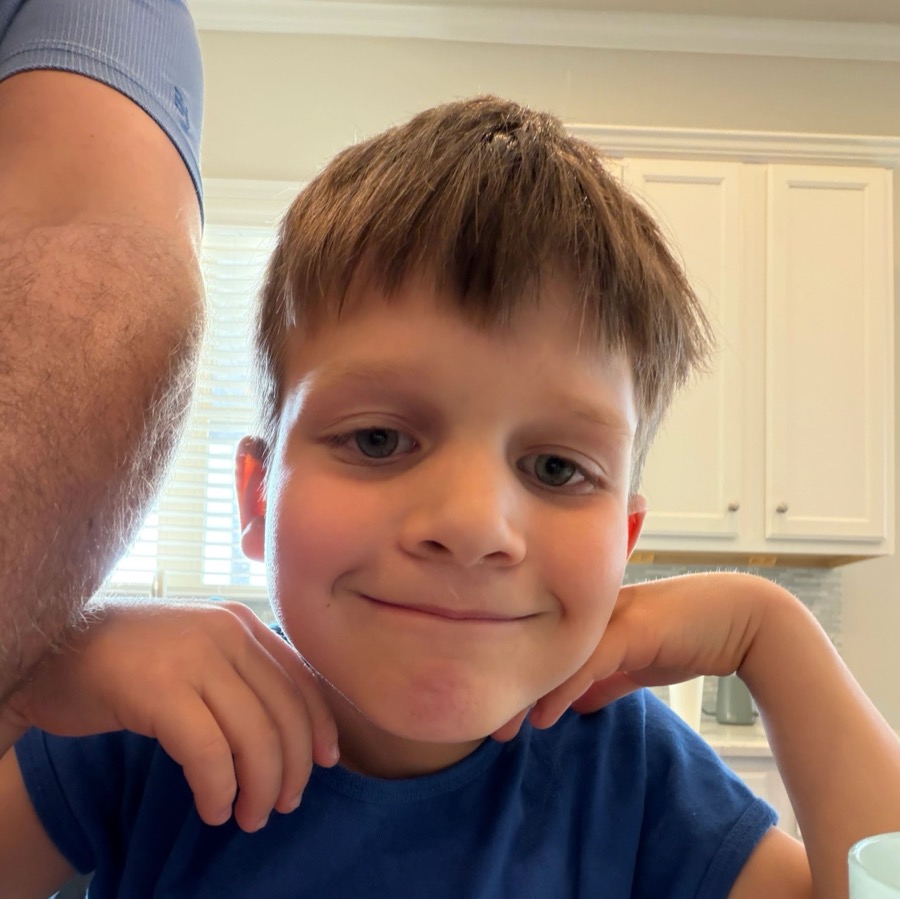 Young boy smiling with his hand on his cheek in a kitchen.