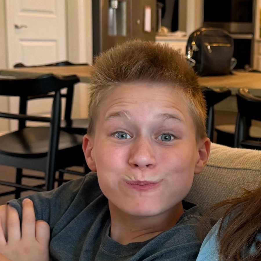 A young boy with blond hair sitting indoors, looking directly at the camera.