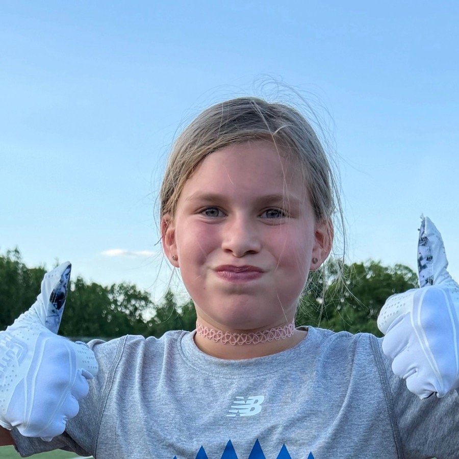 Young girl giving two thumbs up outdoors on a sunny day.